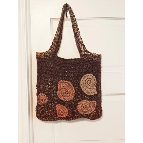 Crocheted brown tote bag with spiral shell-like decorations in lighter shades.