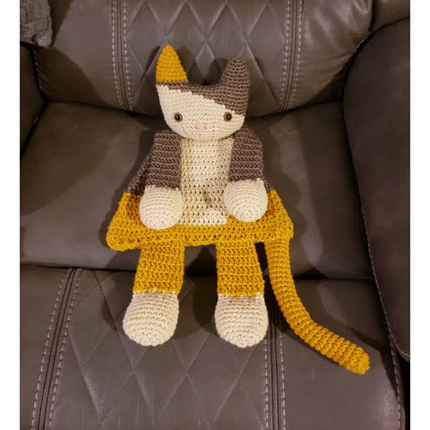 Crocheted cat-like stuffed toy with gray, yellow, and white yarn.
