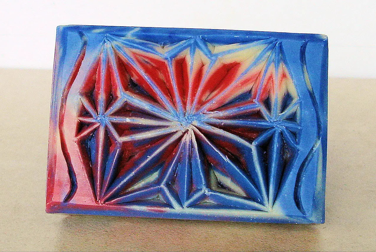 Colorful geometric soap bar with intricate carved patterns in red and blue hues.
