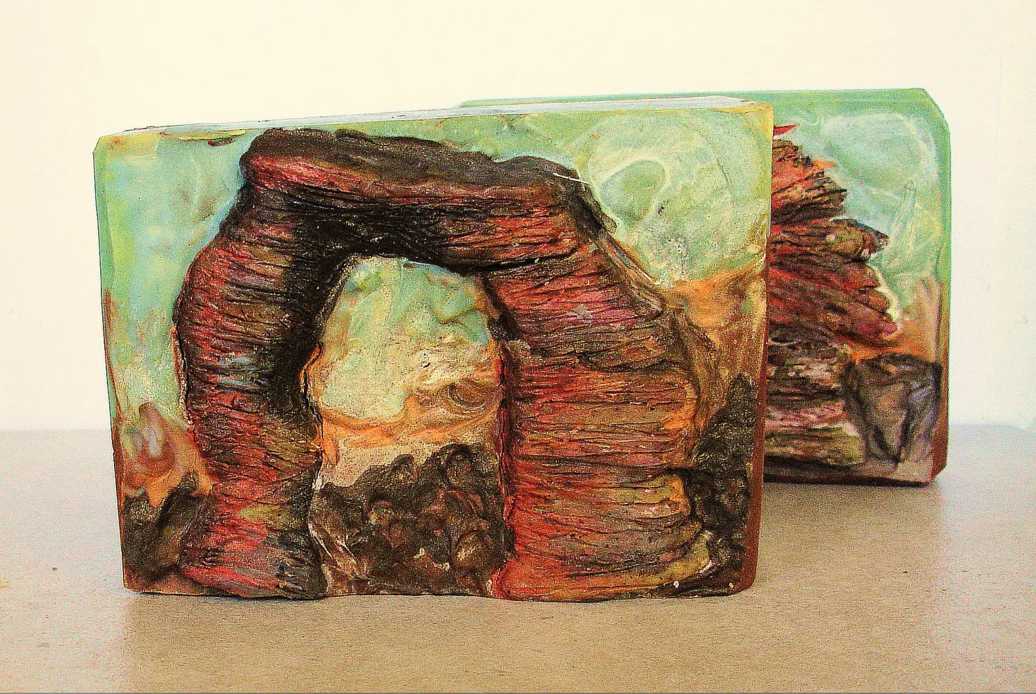Handmade soap bar with a colorful rock arch design embedded within it.
