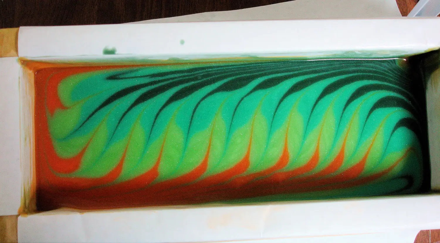 Swirling pattern of green and orange fluid in a rectangular container.