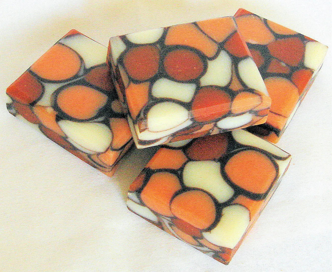 Colorful mosaic-patterned soap bars with circular and irregular shapes in orange, red, and cream tones.