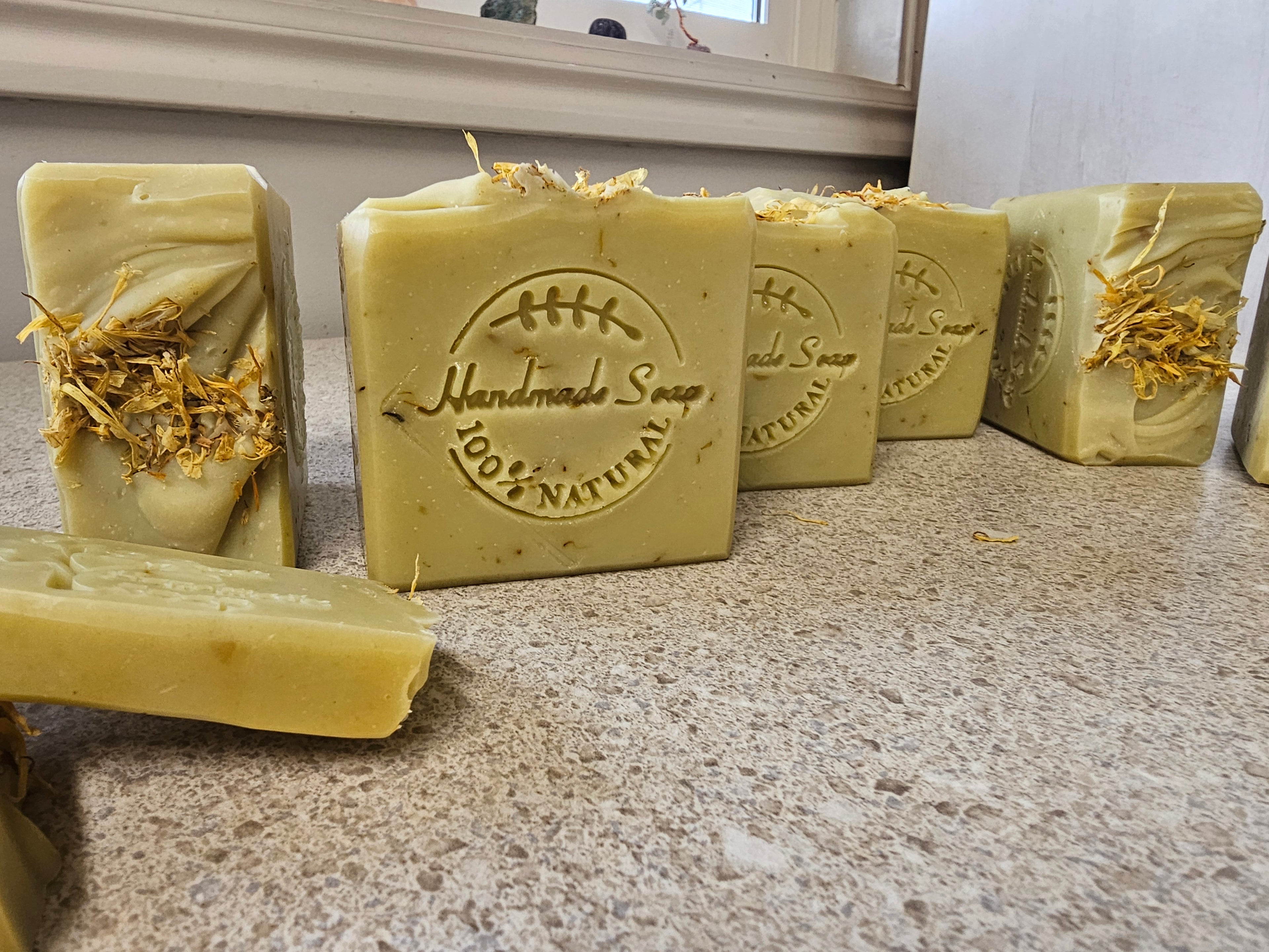 Yellow cold process herbal soap made with calendula flowers that is stampled 100% natural soap and has calendula petals in the soap and on the soap tops. Multiple bars shown, top, front view of soaps.