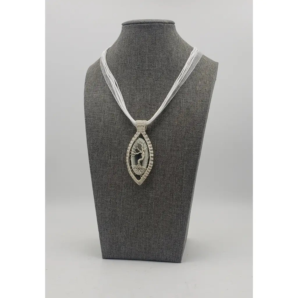 Elegant pendant necklace featuring a silver-toned oval design with a tree of life motif on a white cord.