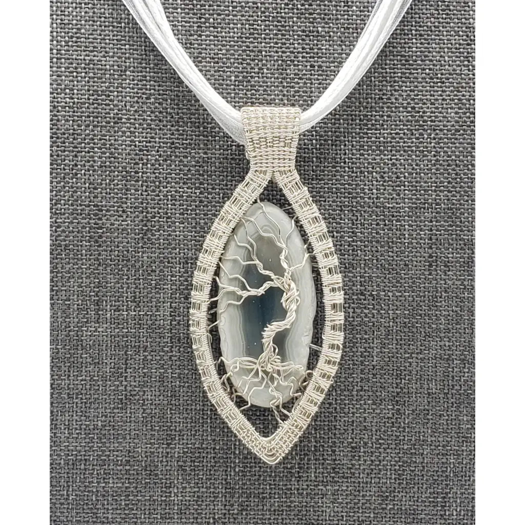 Elegant pendant necklace featuring a silver-toned oval design with a tree of life motif on a white cord.