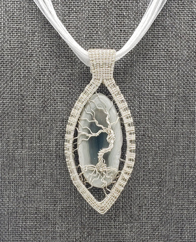 Elegant pendant necklace featuring a silver-toned oval design with a tree of life motif on a white cord.