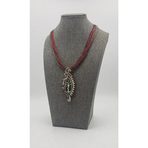 Ornate silver pendant on a burgundy ribbon necklace displayed on a gray jewelry bust.