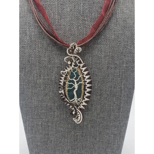 Ornate silver pendant on a burgundy ribbon necklace displayed on a gray jewelry bust.