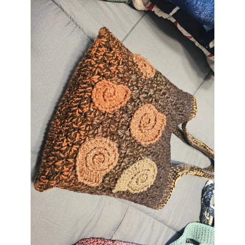 Crocheted brown tote bag with spiral shell-like decorations in lighter shades.