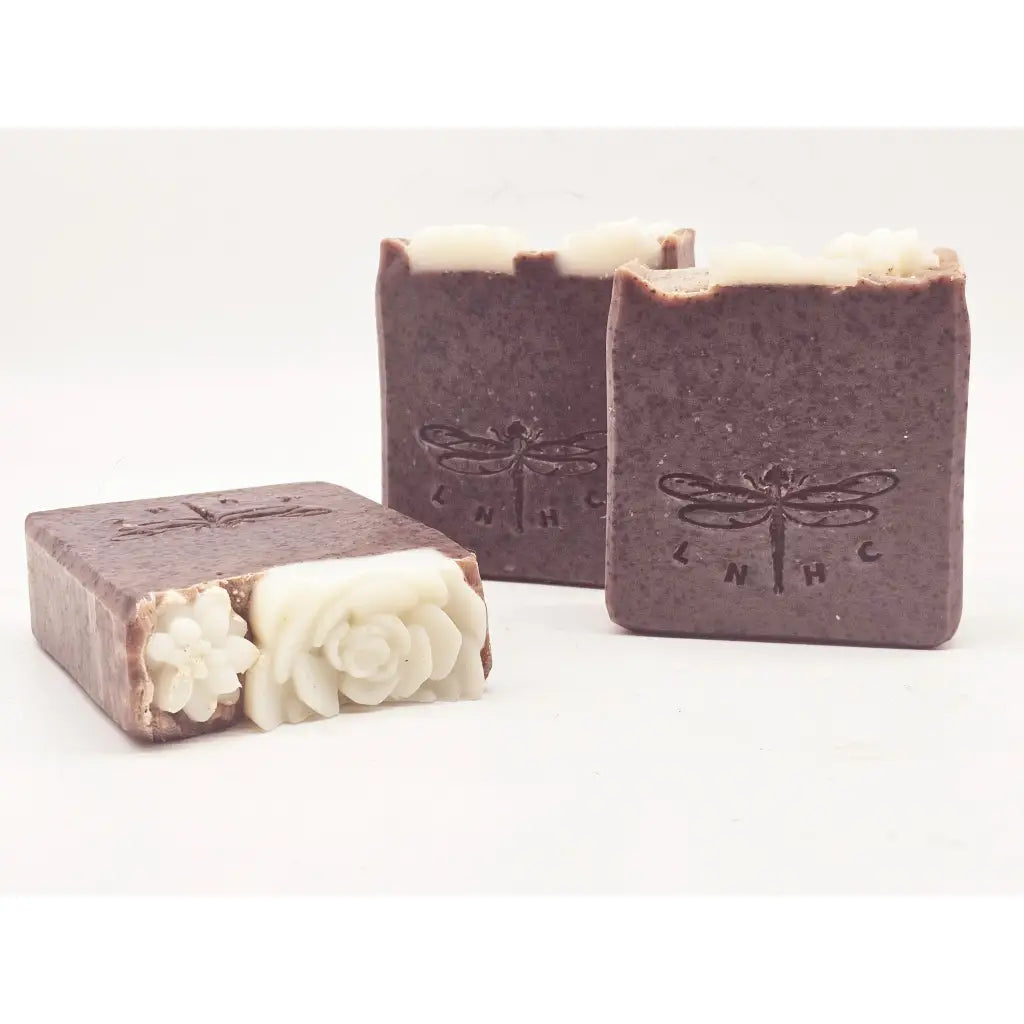 Handmade soap bars with dragonfly imprints and decorative floral designs.