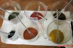 Colorful liquids in measuring cups with whisks for cold process soap at Arches National Park