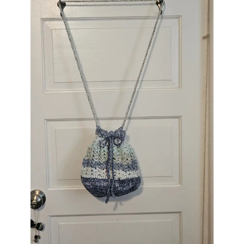 Crocheted drawstring bag with blue and white striped pattern hanging from a chain strap.