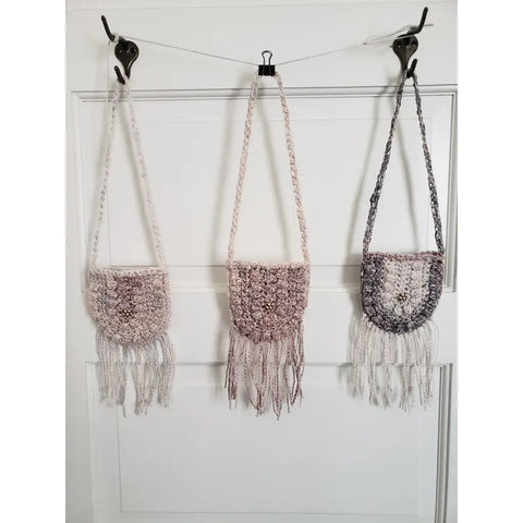 Three crocheted boho-style handbags with fringes hanging from hooks.