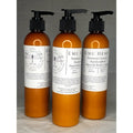 Three amber-colored bottles of EMU Hemp premium luxury hand and body lotion with pump dispensers.
