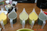 Five pitchers of liquid soap in green and yellow shades for Lisas Natural soap challenge