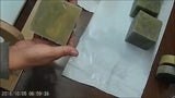 Hand placing olive-green soap bar on white paper for Lisas Natural soap challenge with wood grain technique