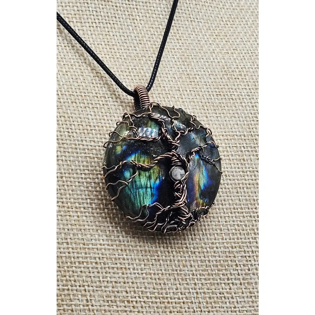 wire wrapped Labradorite & Copper Tree of Life Pendant with a selentie stone bead in the trunk. Side view of the pendant on a beige display.