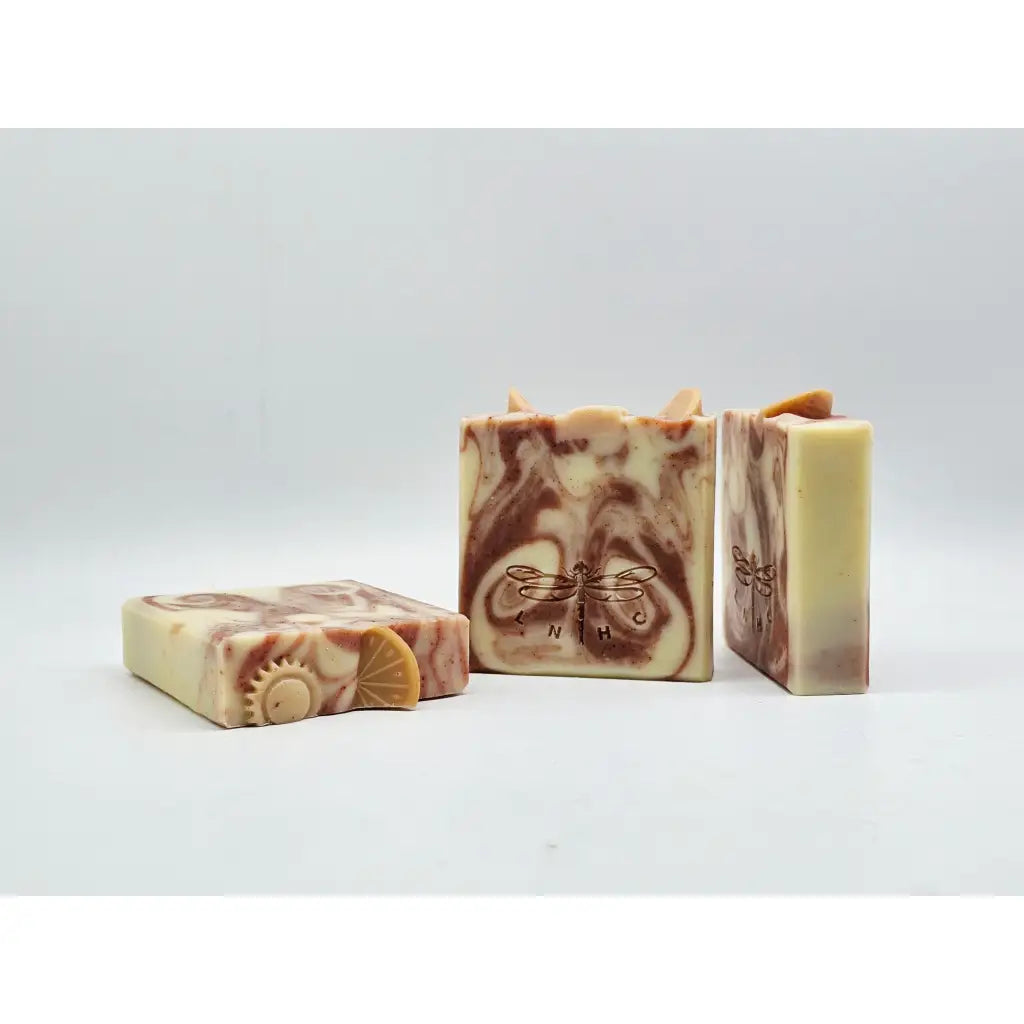 Orange Essential Oil Soap natural soap bars (3) with soap flowers and orange slices on the top. The face of the soap shows dark red-orange swirls and is stamped with a dragonfly