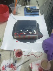 Acrylic string pull device covered in dark liquid with red drips for natural herbal creations