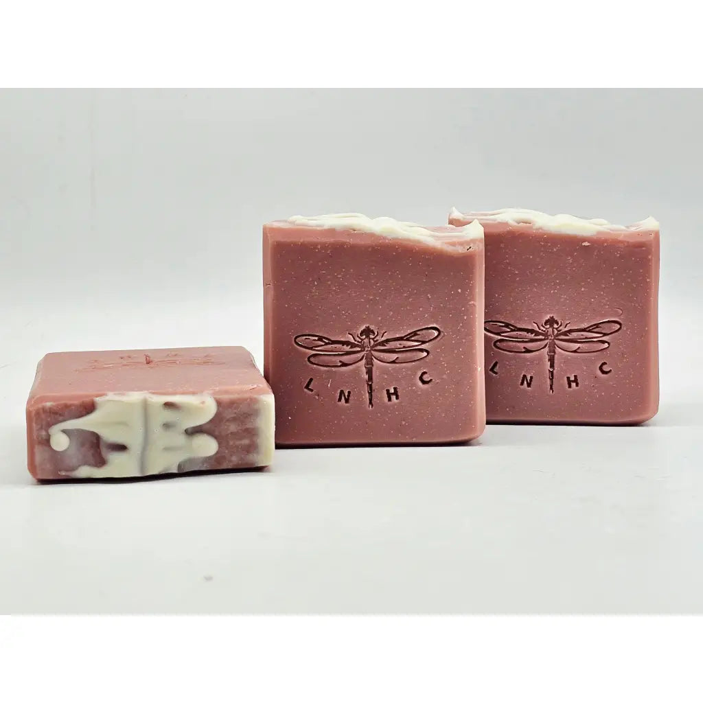 Three dusty pinkrose geranium essential oil soap bars with dragonfly emboss. The top of the soap has a white soap swirl. Top and front view of soaps.
