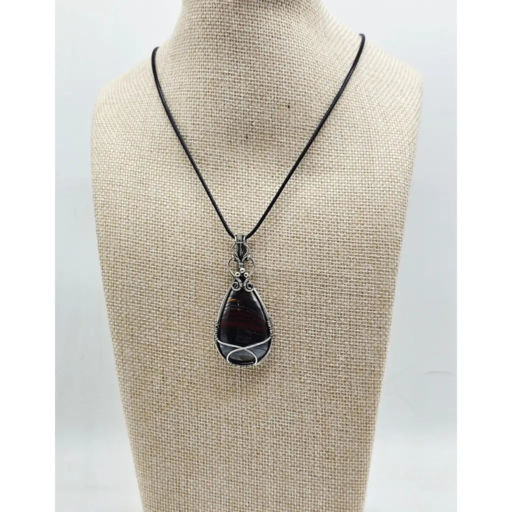 The Earth-Core Sentinel - pendant has a teardrop tiger iron cabachon intricately wire wrapped in sterling silver. front view on a display