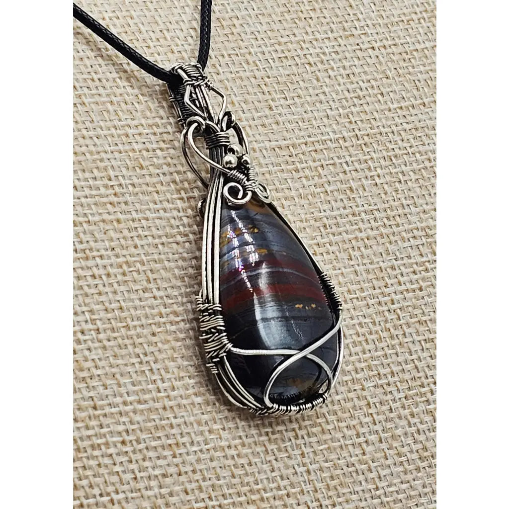 The Earth-Core Sentinel - pendant has a teardrop tiger iron cabachon intricately wire wrapped in sterling silver. side view.
