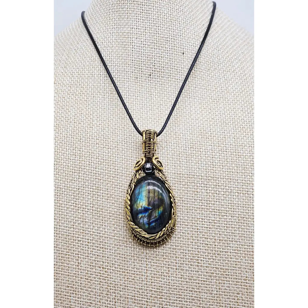 Handmade wire wrapped Labradorite & Red Brass pendant on a cord. High labradorescense showing on the labradorite. Scrolling Brass Braided wire with a hematite accent bead. Front view on a beige display form.