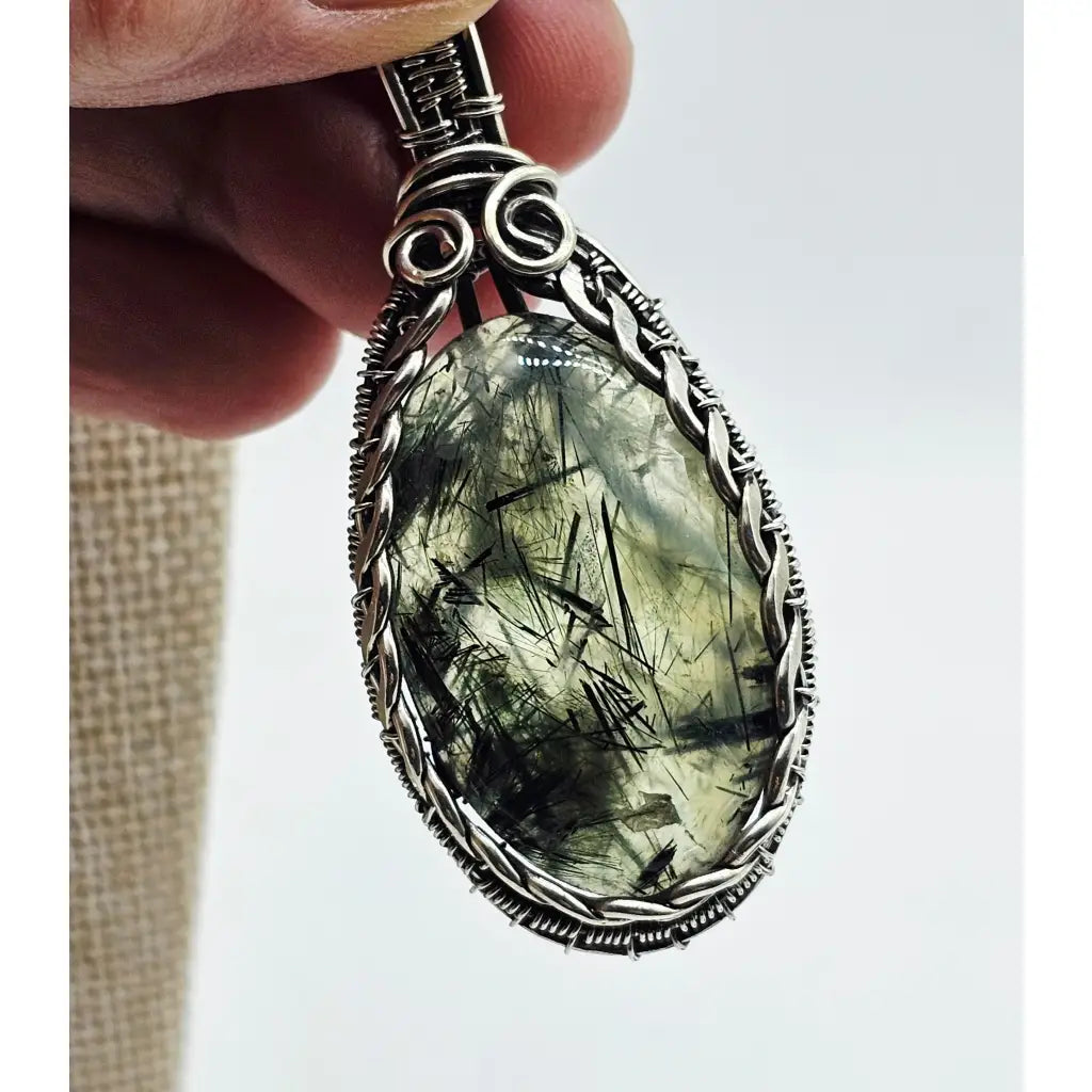 Tourmalinated prehnite pendant in sterling silver wire wrapping, showing the transparency of the stone so you can see the black tourmaline needle inclusions