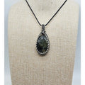 Tourmalinated prehnite pendant in sterling silver wire wrapping.   Front view of a pale green gemstone with black tourmalinated inclusions.