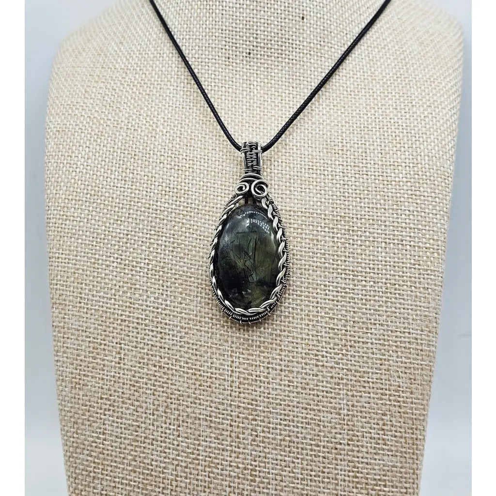 Tourmalinated prehnite pendant in sterling silver wire wrapping.   Front view of a pale green gemstone with black tourmalinated inclusions.